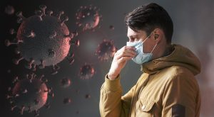 איש עם מסיכה נגד קורונה עומד ומחזיק את האץ מול חיידקים אדומים של וירוס הקורונה